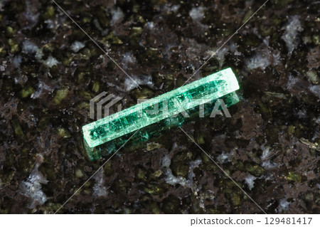 sample of rough emerald crystal on black granite 129481417