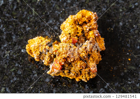 sample of raw wulfenite rock on black granite 129481541
