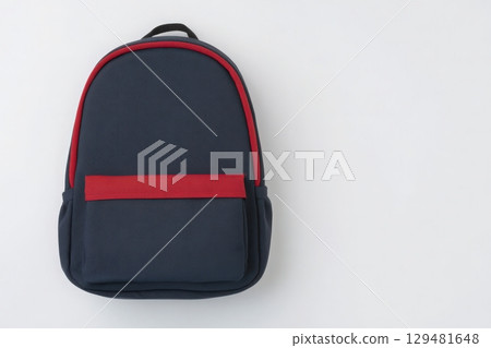 A navy blue backpack with a bold red front pocket is centered on a plain white surface. The design features a simple and modern aesthetic, suitable for school or travel use. 129481648