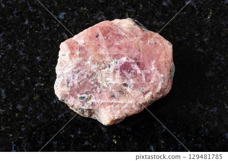 sample of rough pink ruby mineral on black granite 129481785