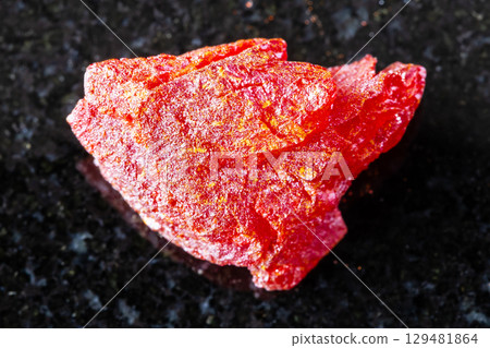 sample of raw realgar mineral on black granite 129481864
