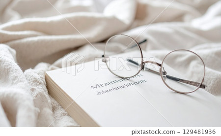 Reading glasses and a book on mindfulness placed on a soft blanket 129481936