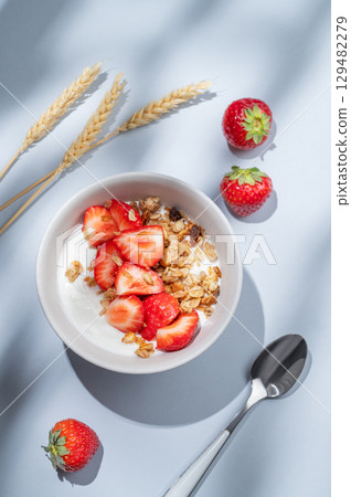 Granola or muesli with natural greek yogurt, strawberry in a bowl on a blue background with wheat Granola or muesli with natural greek yogurt, strawberry in a bowl on a blue background with wheat 129482279