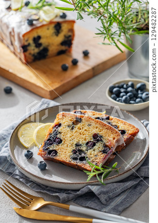 Pieces of homemade blueberry lemon cake on a plate on a light background with fresh berries 129482287