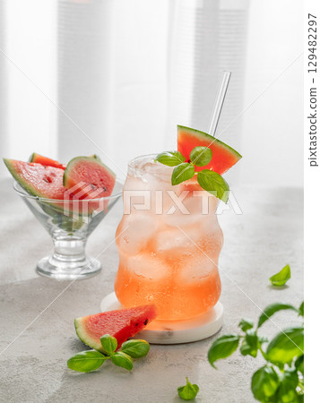 Watermelon mojito cocktail with ice and mint in a glass on a light table near window with slices Watermelon mojito cocktail with ice and mint in a glass on a light table near window with slices 129482297