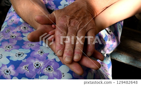 Closeup hands of great grandmother holding small hand of her great grandchild between old wrinkled hand palms 129482648