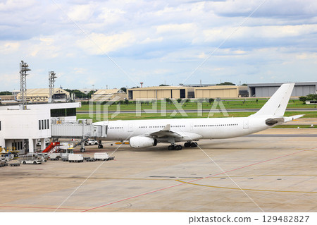 White commercial airplane parking at passenger gate, connect to gate with jet bridge. Being service by ground service team. 129482827