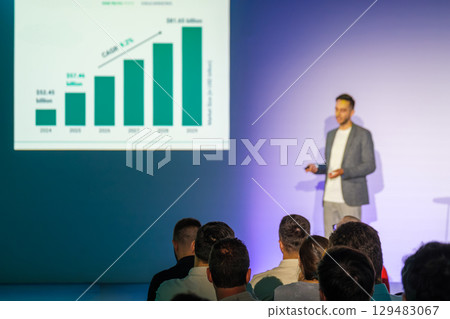 Speaker presenting growth graph to audience in business conference setting Speaker presenting growth graph to audience in business conference setting 129483067