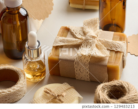 Handmade body care items, natural soap, wrapped in kraft paper and decorated with a crocheted ribbon. Around are placed bottles of oil and other details for decoration 129483213