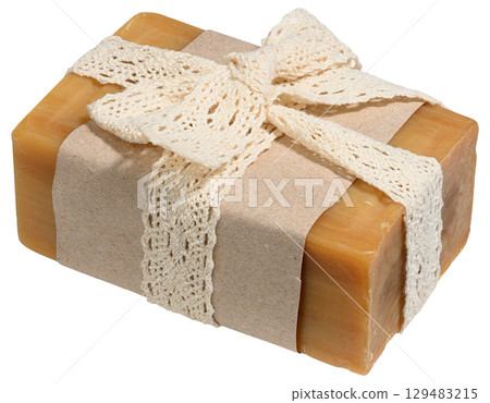 A piece of natural brown soap wrapped in craft paper and tied with a light knitted ribbon tied in a bow. Isolated background 129483215