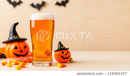 Halloween beer glass with pumpkin decorations, candy corn, and spooky bats on a festive holiday background. 129483357