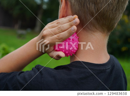 Photo from the back. The boy relaxes his neck muscles with a massage ball, running his hand over his neck. 129483638