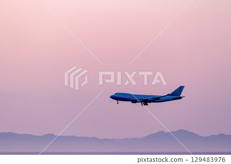 Passenger plane silhouette flying in the pink sunset sky 129483976