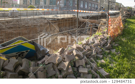 Excavated section of street during repair of underground heating system, surrounded by temporary fence. Pile of construction debris in the foreground 129484731