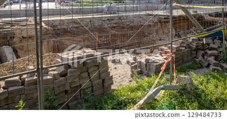 Excavated section of street during repair of underground heating system, surrounded by temporary fence. Pile of construction debris in the foreground Excavated section of street during repair of underground heating system, surrounded by temporary fence. Pile of construction debris in the foreground 129484733