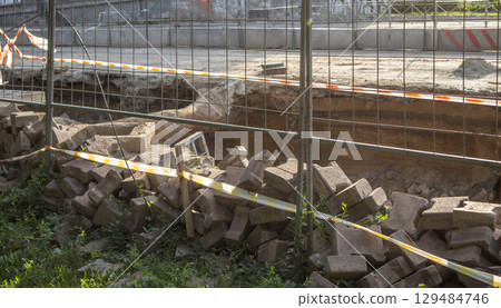 Excavated section of street during repair of underground heating system, surrounded by temporary fence. Pile of construction debris in the foreground Excavated section of street during repair of underground heating system, surrounded by temporary fence. Pile of construction debris in the foreground 129484746