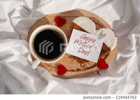 Flat lay top view HAPPY MOTHER'S DAY message on paper card Morning breakfast in bed in wooden tray Present gift idea Valentine's Day Holiday celebration Heart shaped croissants. Puff pastry new trendy 129484762