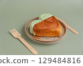Heart shaped pistachio croissant on plate with recycled fork and knife on green background with copy space. Puff pastry trendy sweet dessert bakery. Creamy dough experiment  129484816