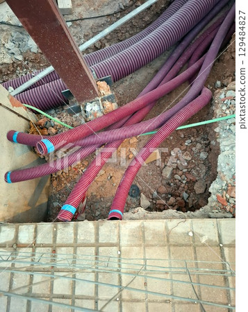 Many red plastic pipes are laid out in a construction site, ready for installation as part of the communication system. The groundwork indicates ongoing infrastructure development. 129484827
