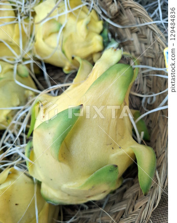 Golden yellow pitahaya fruit showcases its unique shape and texture, surrounded by natural straw in a market setting. Perfect for culinary exploration and tropical enjoyment. 129484836