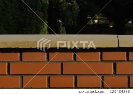 View of the brick base. Brick exterior wall with white finished top with polished white capstone. Brick base. Brick background with polished top with headstone. Building and construction concept. 129484888