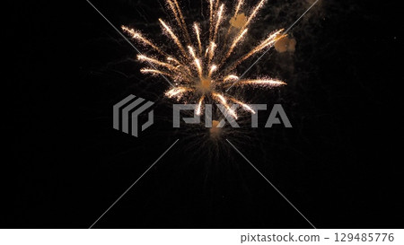 Fireworks bursts paint dark evening sky with vivid colors on holiday party. Exploding display of fireworks with flying lights in dark sky. Sparkling canopy at festive fireworks show at night 129485776