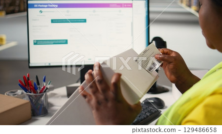 Black woman packing goods and applying shipping labels on boxes, creating awb tracking numbers on tags for easy distribution. Worker using adhesive airway bill stickers. Camera A. Black woman packing goods and applying shipping labels on boxes, creating awb tracking numbers on tags for easy distribution. Worker using adhesive airway bill stickers. Camera A. 129486658