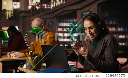 Woman listens to loud music on headset and disturbing other people in the library, senior man asking her to keep the volume low, breaking the library rules. Careless person singing. Woman listens to loud music on headset and disturbing other people in the library, senior man asking her to keep the volume low, breaking the library rules. Careless person singing. 129486675