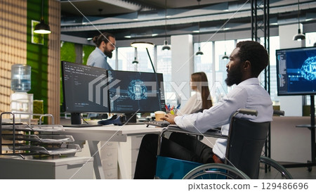 IT professional in wheelchair in inclusive office developing software applications using AI automation. Computer scientist with paraplegia debugging applications with artificial intelligence, camera A 129486696