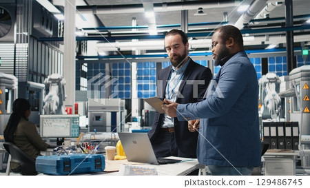 Diverse team of engineers and specialists collaborate in a solar panel factory, review blueprints and share ideas to enhance renewable energy production and sustainable innovation. Camera A. Diverse team of engineers and specialists collaborate in a solar panel factory, review blueprints and share ideas to enhance renewable energy production and sustainable innovation. Camera A. 129486745