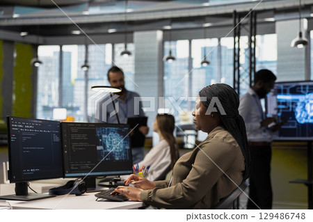 System administrator in tech startup uses AI on PC to optimize performance and forecast issues. African american woman in office training machine learning models using computer 129486748