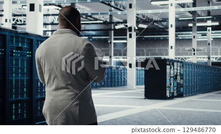 Engineer walking in server farm, automating system diagnostics using machine learning predictions. IT specialist working in data center using notebook to configure gear for AI tasks, camera A Engineer walking in server farm, automating system diagnostics using machine learning predictions. IT specialist working in data center using notebook to configure gear for AI tasks, camera A 129486770