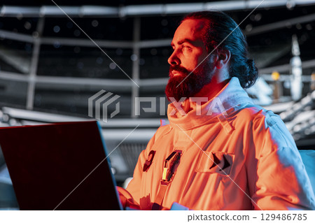 Astronaut works on notebook to troubleshoot red light warning triggered by system error in orbital station. Spaceship crew member using device to investigate malfunction affecting operations 129486785