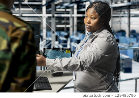 Team of soldiers in uniform confirming target locations using aerial image overlay on monitor. African american military units in server hub gathering strategic terrain data via satellite systems 129486790
