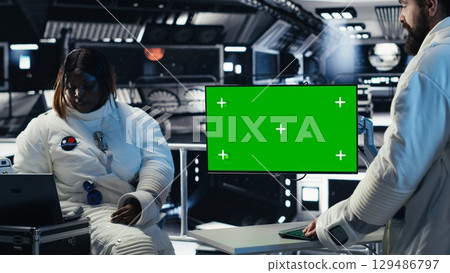 Researchers flying together in starship, looking at green screen monitor, exploring Mars. Cosmonauts using mockup display to ensure operational readiness before landing on red planet Researchers flying together in starship, looking at green screen monitor, exploring Mars. Cosmonauts using mockup display to ensure operational readiness before landing on red planet 129486797