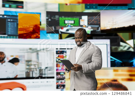 Smiling person uses tablet, streaming online video content during leisure time in modern digital environment. Joyful man browses social media app in front of digital backdrop displaying clips collage 129486841