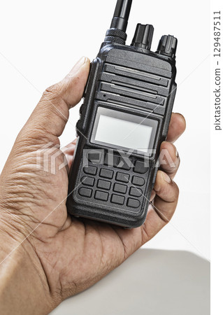 Closeup view of a human hand holding a black walkie talkie radio communication device isolated over a white background Closeup view of a human hand holding a black walkie talkie radio communication device isolated over a white background 129487511