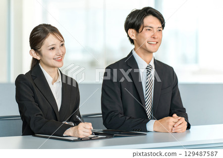 Businessmen and businesswomen in suits standing at a desk (interviewer, company information session) 129487587