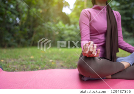 Woman in a sporty outfit is relaxing and meditating zen-like on a fitness mat in a public park outdoors. Concept of a Healthy active lifestyle 129487596