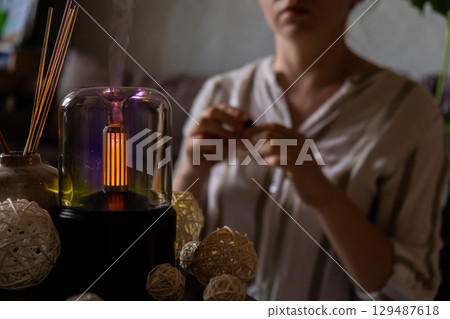 Female hands adding essential oil to Close up of home perfume scent air humidifier with light. Aromatherapy holistic health practices concept. Stress relief activities preparing for meditation. Simple 129487618