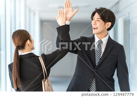Young businessmen and women exchanging high fives as they pass each other in an office corridor Young businessmen and women exchanging high fives as they pass each other in an office corridor 129487779