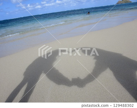 A heart-shaped shadow formed by a man and woman's arms cast on the sand of Hawaii's Lanikai Beach. Campaign advertisements and event announcements. 129488302