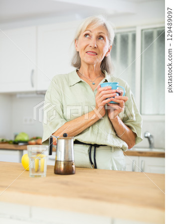 Relaxed elderly woman drinking coffee at kitchen Relaxed elderly woman drinking coffee at kitchen 129489097