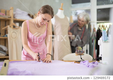 young dressmaker helps a seamstress with sewing clothes young dressmaker helps a seamstress with sewing clothes 129489172