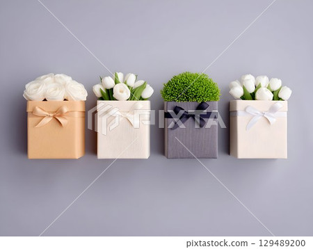 Gift boxes decorated with white roses, tulips, green foliage, neatly arranged on gray surface, ribbons enhancing elegant festive styling Gift boxes decorated with white roses, tulips, green foliage, neatly arranged on gray surface, ribbons enhancing elegant festive styling 129489200