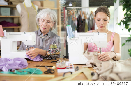 Two seamstresses sitting and working in the workshop 129489217