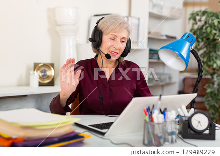 Office worker woman is working at a computer and talking by headset with client in office Office worker woman is working at a computer and talking by headset with client in office 129489229