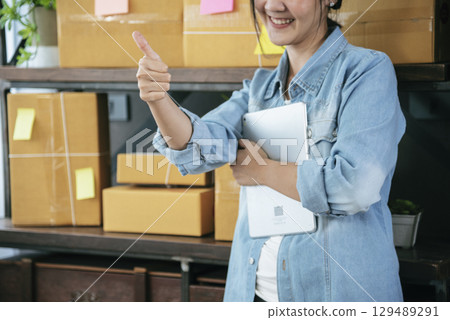 Asian woman startup small business at home office. Online seller entrepreneur young asian woman use tablet checking online order. Woman using tablet check stock goods supply delivery package shipping 129489291