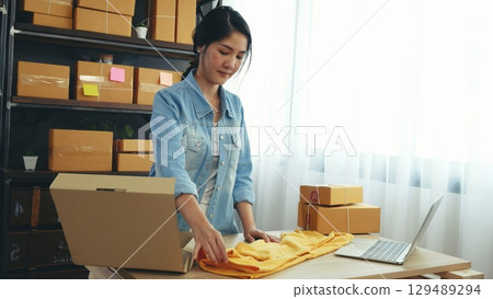 Fashion designer Women packing box on table checking goods quality package. Asian women startup small business at home office desk pack fashion design clothing. Asian woman packing startup business Fashion designer Women packing box on table checking goods quality package. Asian women startup small business at home office desk pack fashion design clothing. Asian woman packing startup business 129489294