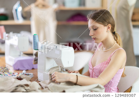 Woman seamstress sews on sewing machine in workshop 129489307